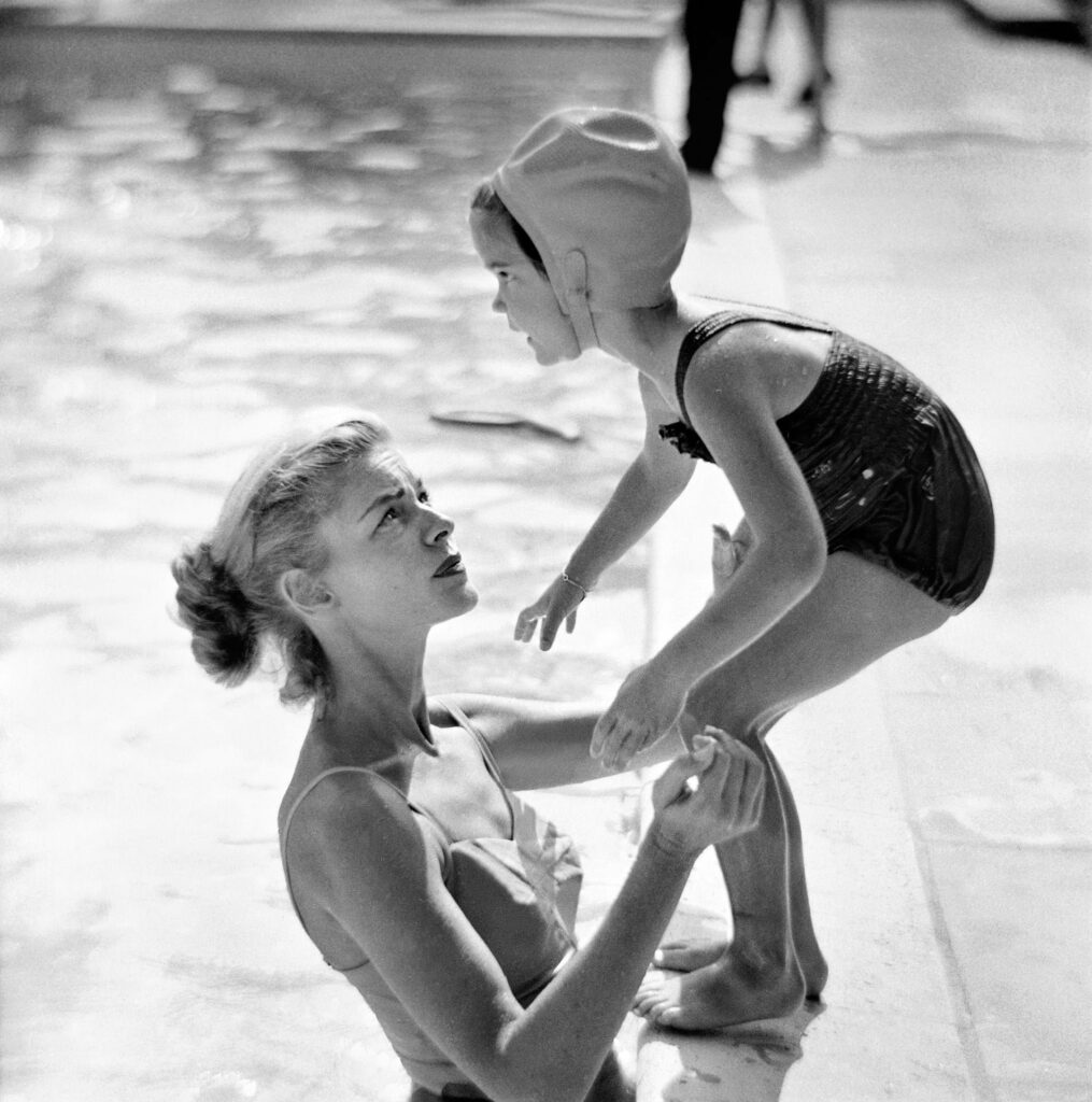 le grand bain. Lauren Bacall and her daughter Leslie photographed by Phil Stern, circa 1955  alt : une petite fille sur le bord de la piscine, en position de plonger, sa mère, debout dans l'eau, la soutient du regard