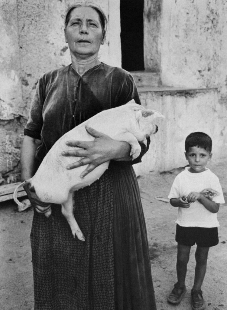 maman me prenait rarement dans ses bras. Lisetta Carmi, Onifai, Sardinia, 1964. un jeune garçon à côté d'une femme portant un porcelet