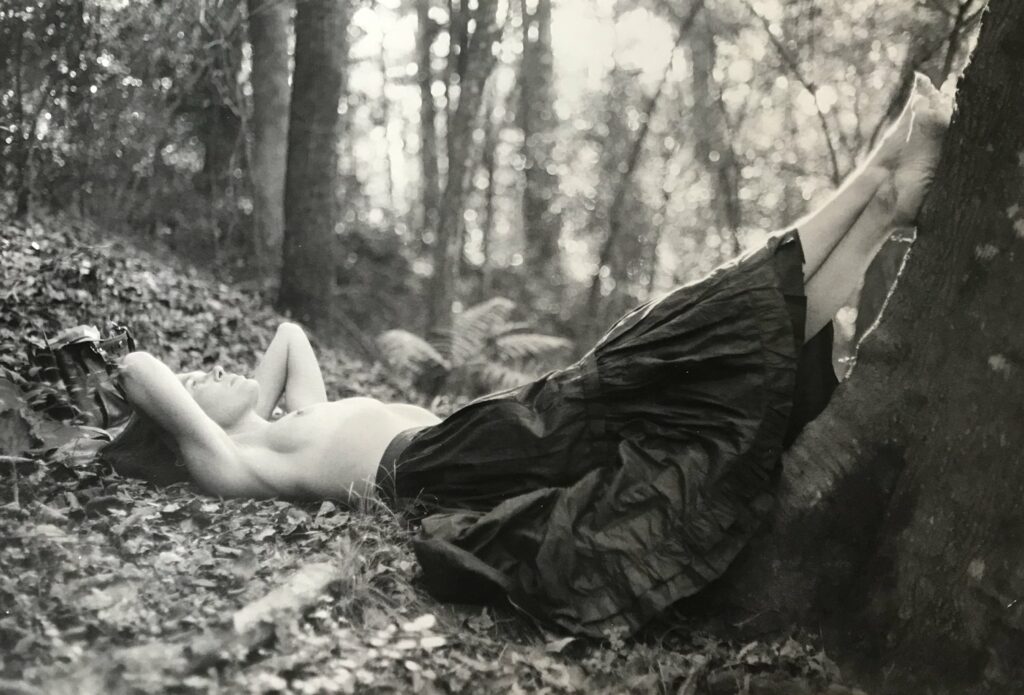 les pieds sur les arbres érotisme. Mary Margaret Hansen Basking in Sunlight. une femme, torse nu, allongée sur le dos en forêt, les mains sous la tête, prend le soleil et appuie ses pieds sur le tronc d'un arbre