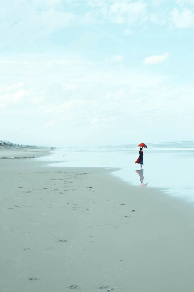 une tache rouge sur le sable bleu. une femme en rouge debout sur la plage