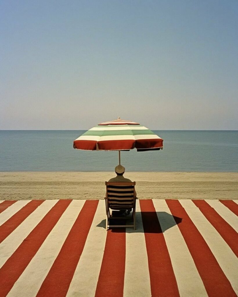 plage privée. Aikaterini Theocharidou. "j'allais au bord de la mer, sans mon père, ma soeur, ma mère" (Michel Jonasz). alt : un homme, au bord d'une mer d'huile, seul sur une plage recouverte d'une toile bicolore assortie à son fauteuil et à son parasol