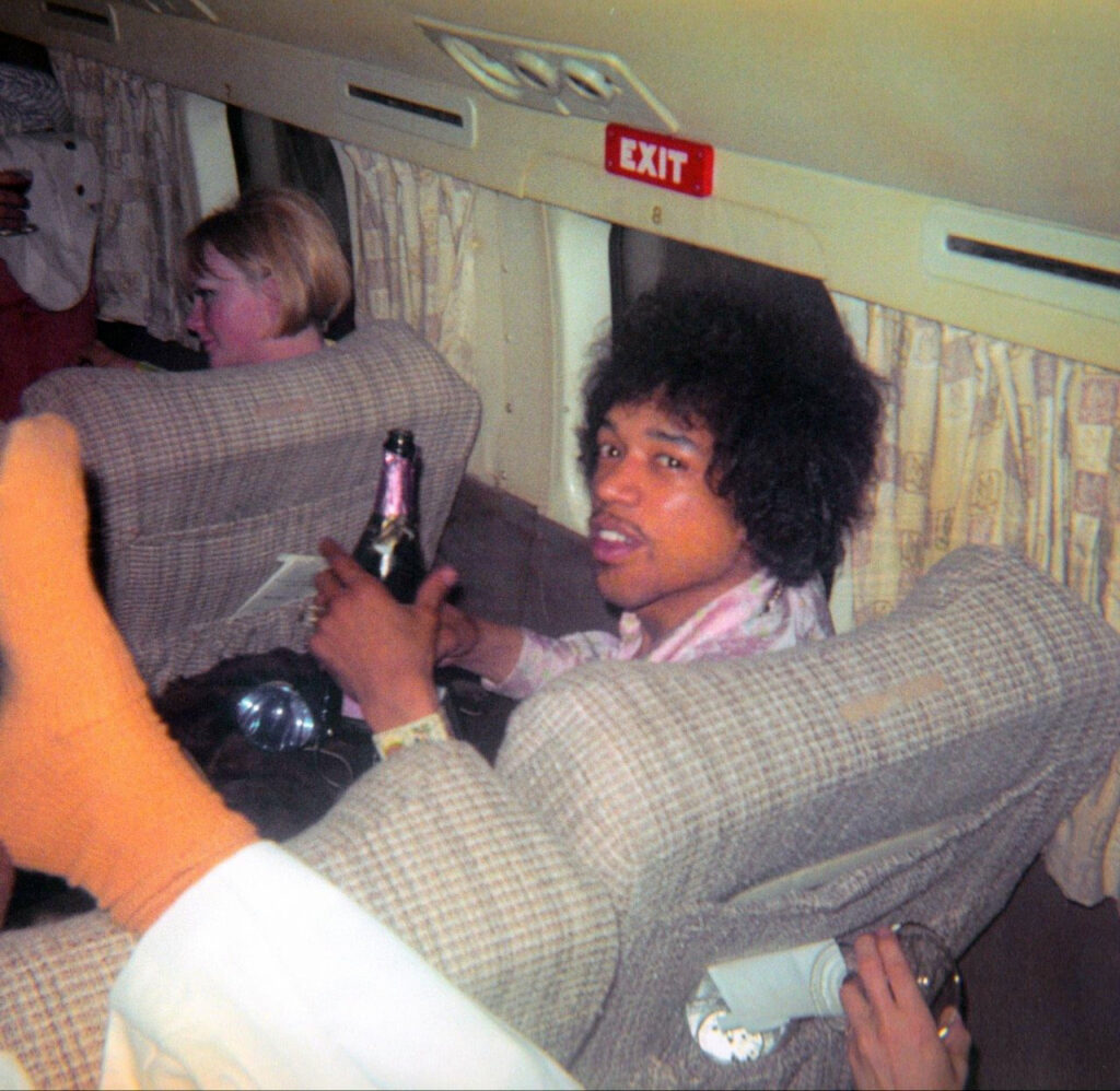 merci de tes voeux d'anniversaire Jimi. non, franchement, ça me touche. alt : Jimi Hendrix portant un toast au champagne à ma santé lors d'un voyage en avion le 17 août 1967